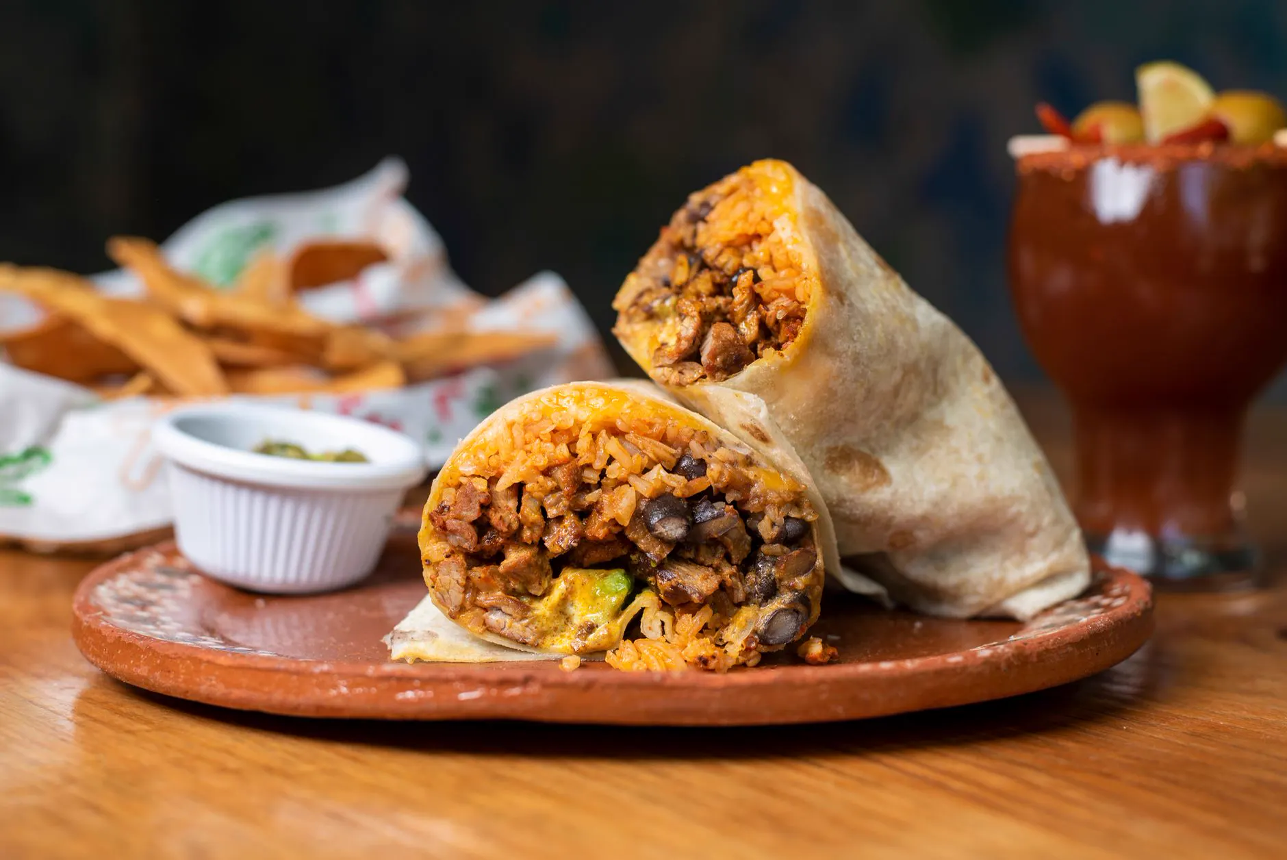 Burrito cut in half on a clay plate with chips and guacamole